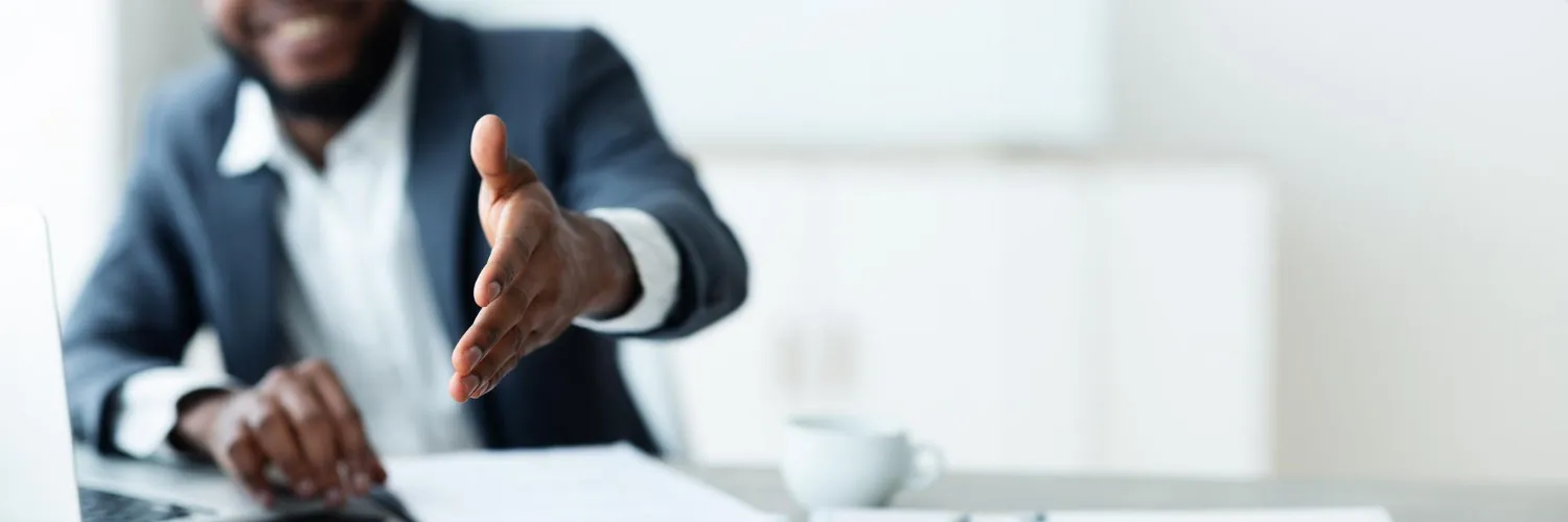 A delegate in a suit extending a hand across a desk in welcome